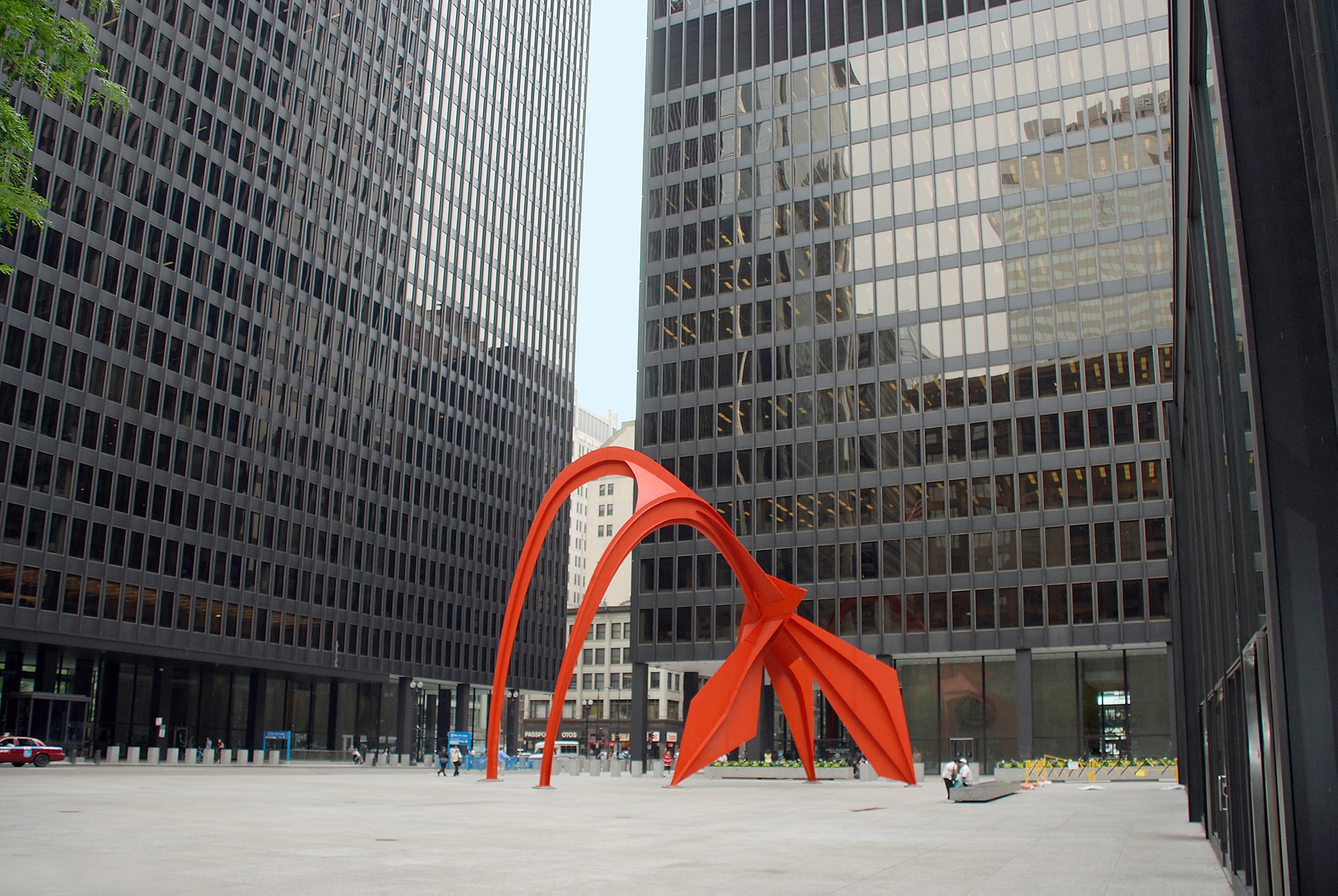 Photo of the Chicago Federal Center Courtyard. Three large, black, modern building surround the sides, with a bright red arched modern sculpture serving as the focal point of the courtyard. Taken by Massiel Lucca-Amador (5P1FB).